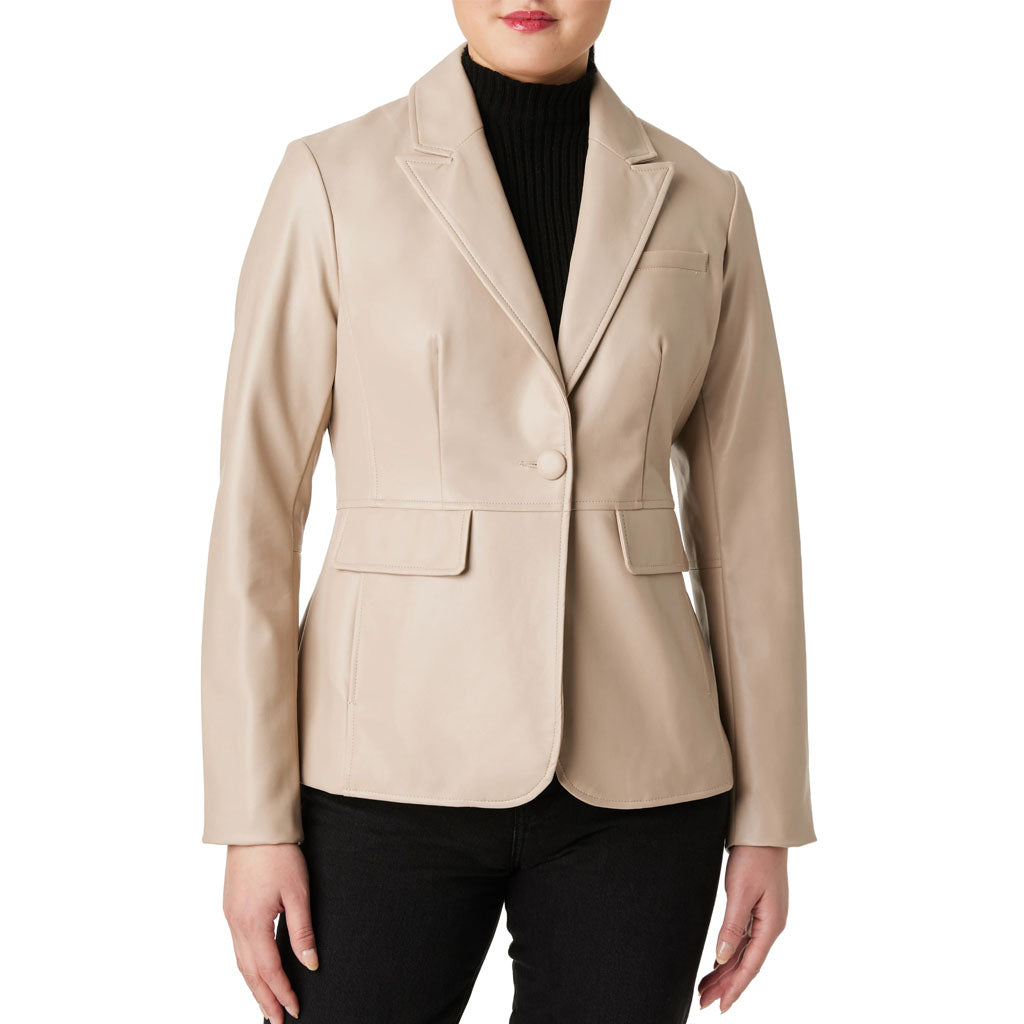 A woman wearing a structured beige faux-leather blazer over a black ribbed turtleneck and black pants, shown from the lips down against a plain white background.
